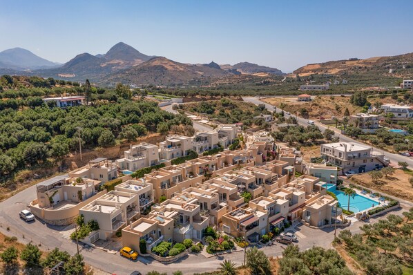 A residential area with modern buildings, a swimming pool, and a mountainous backdrop.