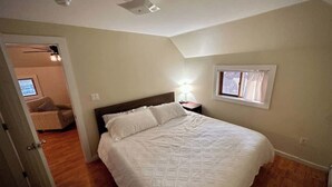 A bedroom with a bed, a nightstand, a window, and a door leading to another room.