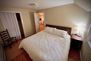 A bedroom with a bed, a chair, a nightstand, and a door leading to another room.