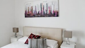 Une chambre d’hôtel avec un lit, deux tables de chevet et une œuvre d’art représentant un paysage urbain accrochée au mur.