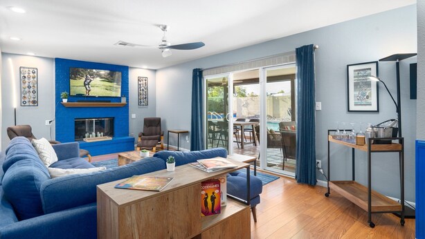 Ein Wohnzimmer mit blauem Sofa, Holztisch, Kamin, Deckenventilator und einer Glastür zum Außenbereich.