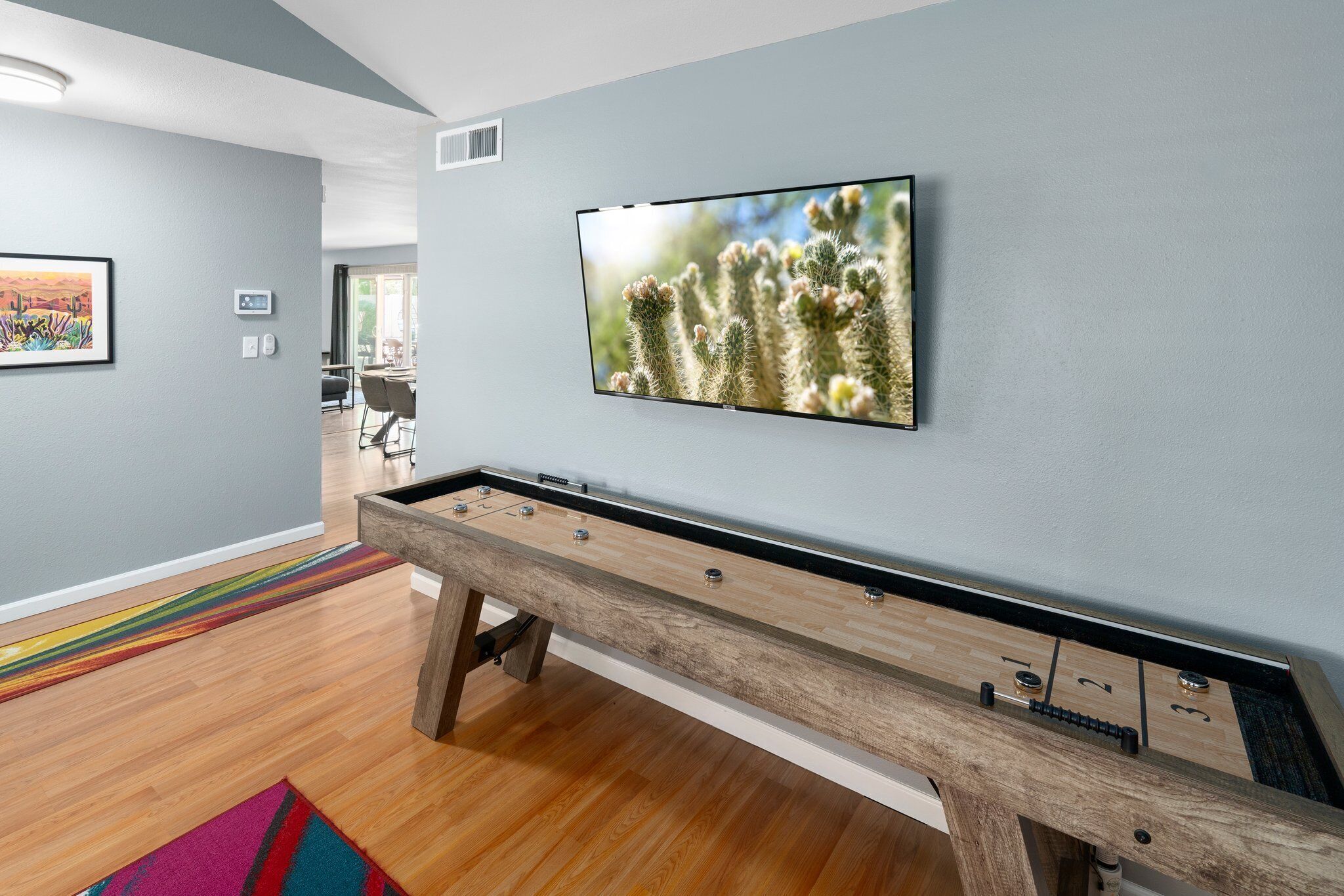 A room with a pool table, a framed cactus picture, and a colorful rug.