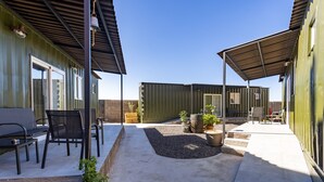 Un espace patio avec des sièges extérieurs, une partie couverte et un bâtiment en conteneur vert portant l’inscription « MOLLA ».