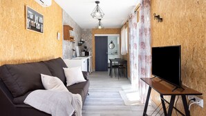 Un salon chaleureux avec un canapé, un téléviseur posé sur un meuble et une cuisine en arrière-plan.