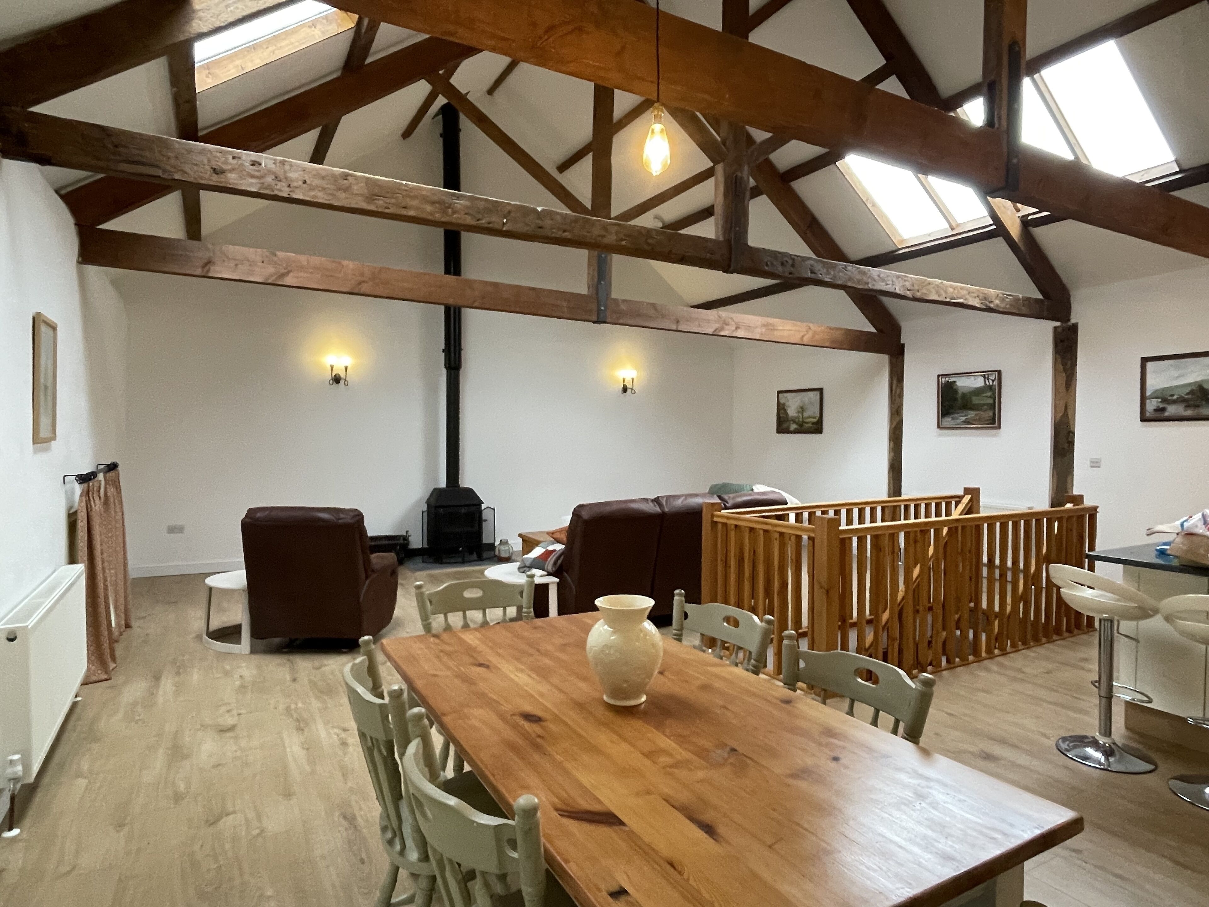 A rustic dining area with a wooden table, chairs, and a vase. There is a fireplace and a high ceiling with exposed beams.