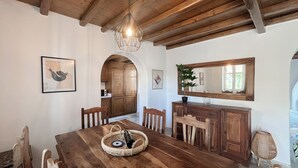 A dining area with a wooden table, chairs, a chandelier, and a mirror above the counter. - Pool House in Ornos (Mykonos)