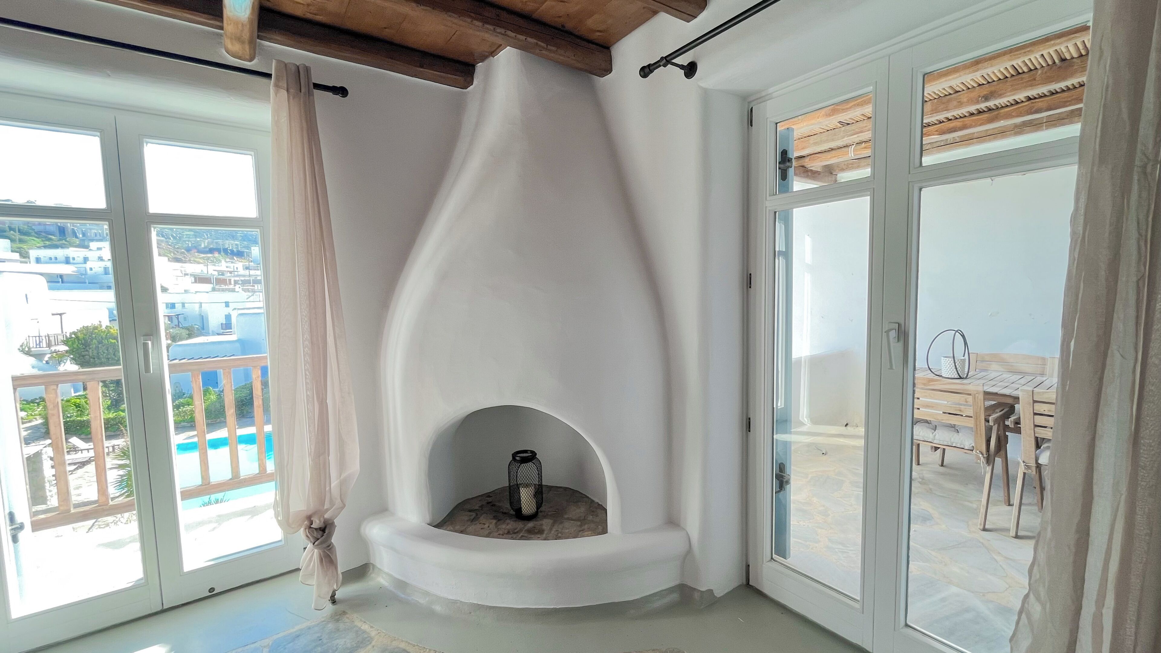 Habitación de esquina con chimenea, ventanas amplias y balcón con mobiliario exterior.