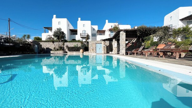 A clear swimming pool with a stone wall and a wooden deck with lounge chairs. - Pool House in Ornos (Mykonos)