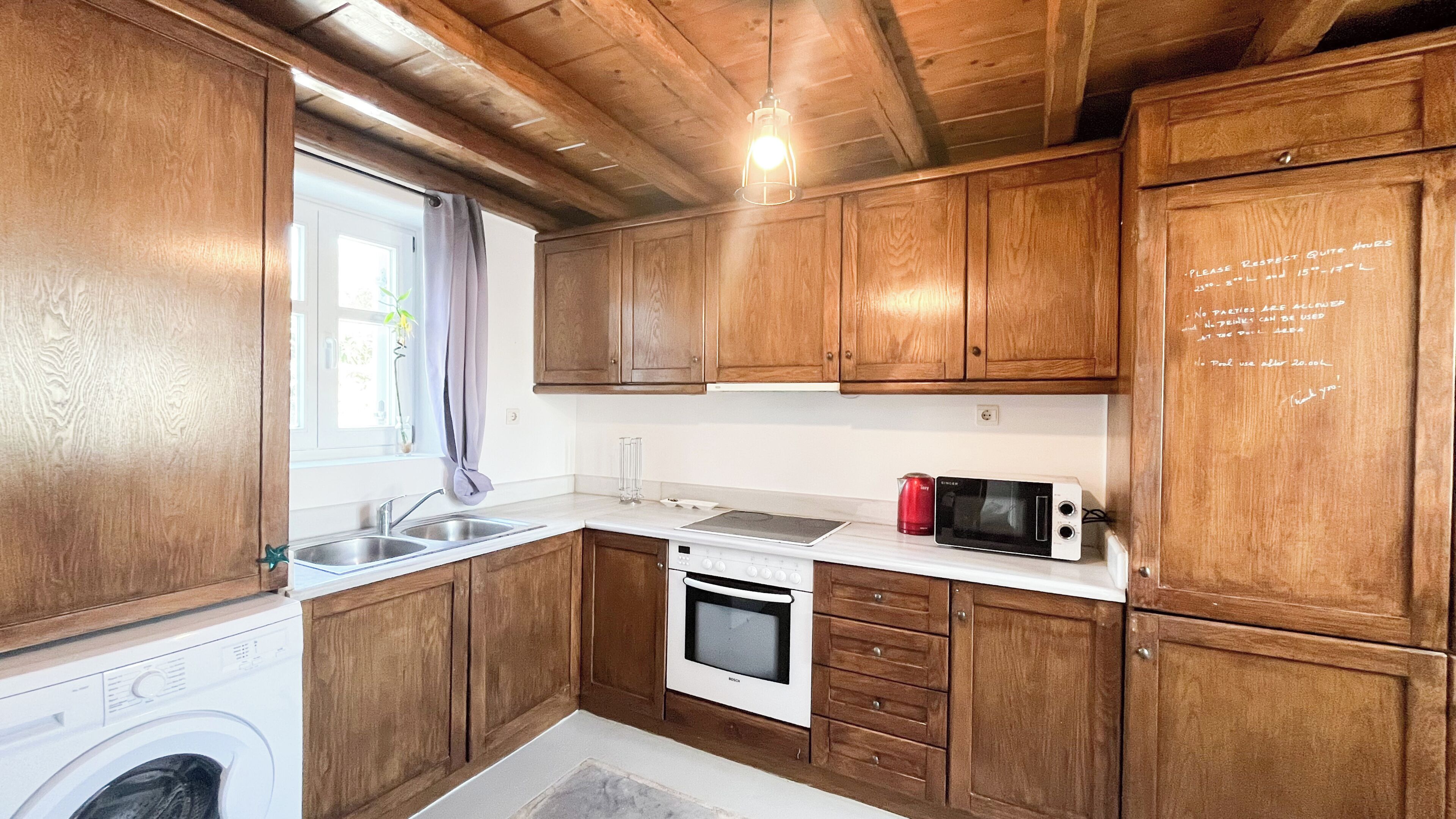 A compact kitchen with wooden cabinets, a microwave, a stove, and a washing machine.