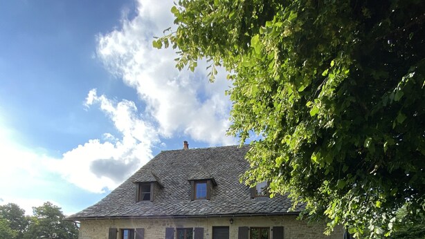 Ein Steinhaus mit Ziegeldach, umgeben von einem Rosengarten mit rosa Rosen.