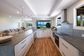 A modern kitchen with a large island, white cabinetry, and a view of the outdoors. - Nautical Views - Airlie Beach (Airlie Beach)