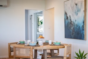 Ein Essbereich mit einem runden Holztisch, Korbstühlen und einem großen abstrakten Gemälde an der Wand.