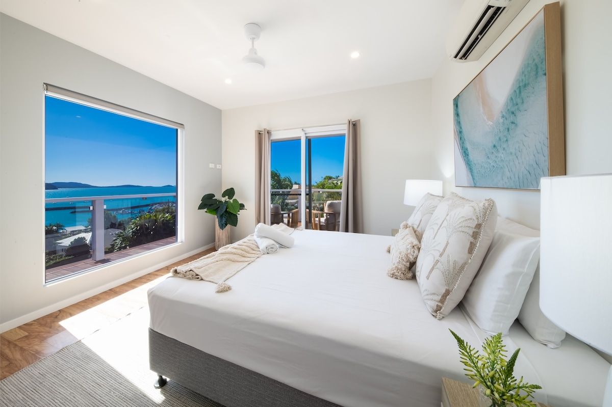 Un dormitorio con una cama grande, vista al mar y un balcón.