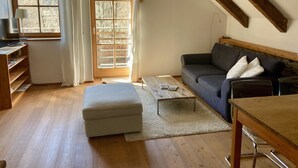 A cozy living room with a sofa, ottoman, coffee table, and a TV on a wooden shelf. - Stylish vacation apartment in an old farmhouse - south view (Kirchbach)