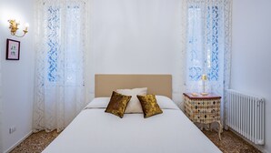 Una camera da letto con un letto, due cuscini, un comodino con una lampada e un termosifone.