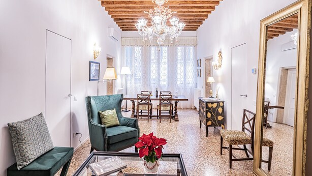 Un ampio soggiorno con soffitto in legno, un lampadario, un'area pranzo con tavolo e sedie e un grande specchio.