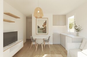 A modern kitchen with white cabinets, a dining area with a round table and chairs, a hanging light fixture, and a framed picture on the wall.