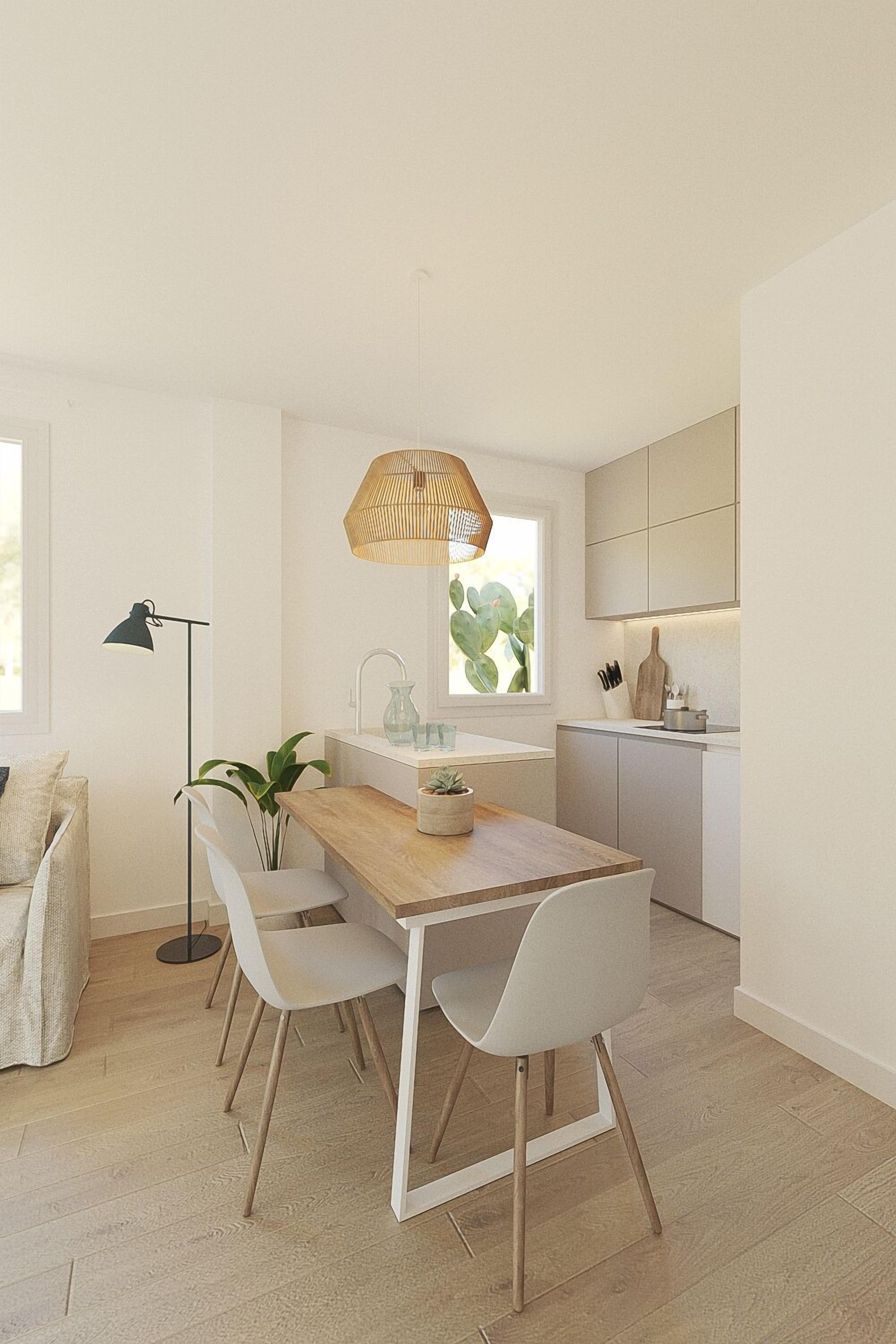 Une cuisine moderne avec une table en bois, des chaises blanches, un luminaire suspendu et une fenêtre agrémentée d’une plante.