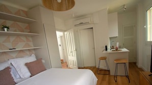 A modern bedroom with a large bed, a small kitchenette, and a bathroom visible in the background. - Lavendel Apartments (Ses Salines)