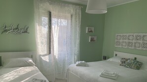 Een hotelkamer met twee bedden, een groot raam met dunne gordijnen, een witte plafondlamp en een wand met decoratieve panelen.