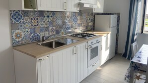 Een kleine keuken met witte kastjes, een betegelde spatwand, een gasfornuis en een koelkast.