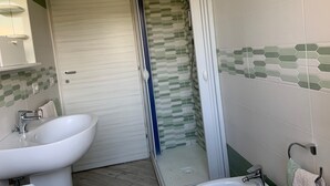 Een badkamer met een witte wastafel, een spiegel en een douche met een betegelde wand in groen en wit.