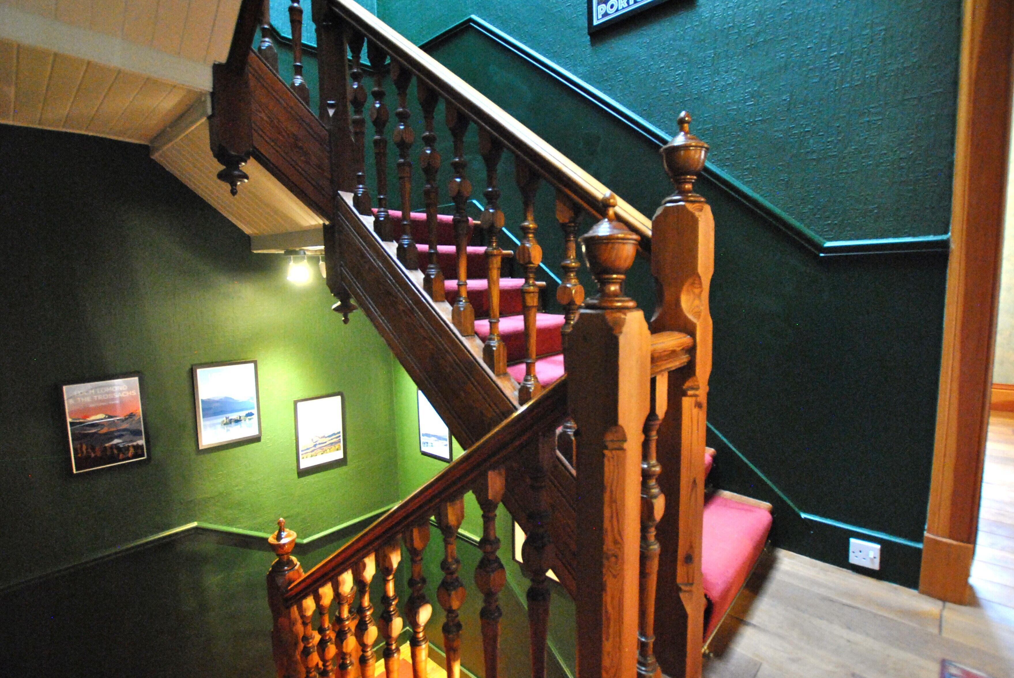 A wooden staircase with a handrail, green walls, and a pink carpeted landing.