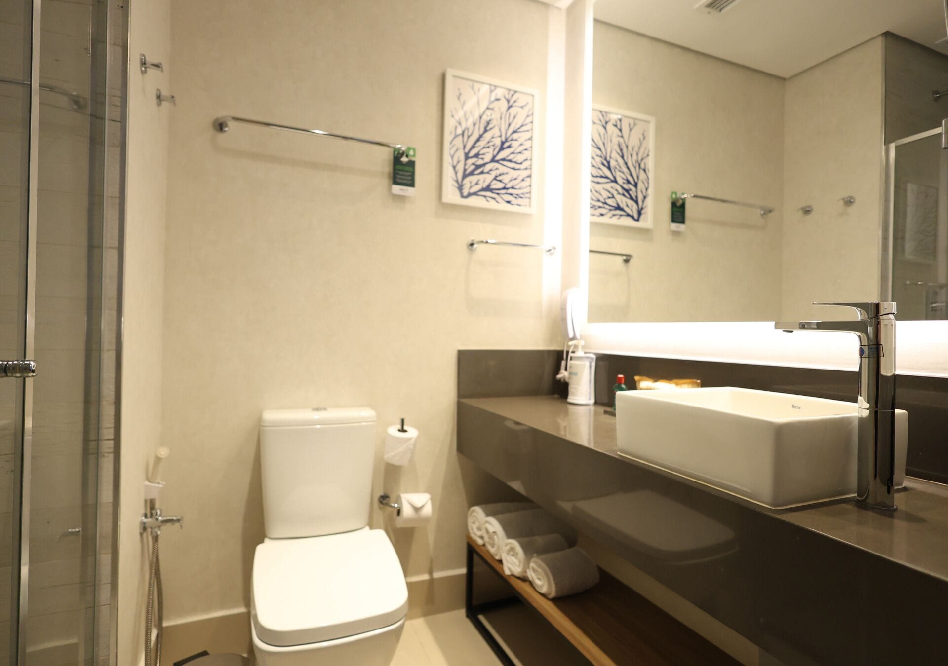 A modern bathroom with a toilet, sink, and shower. There are towels on a shelf and a towel rack on the wall.