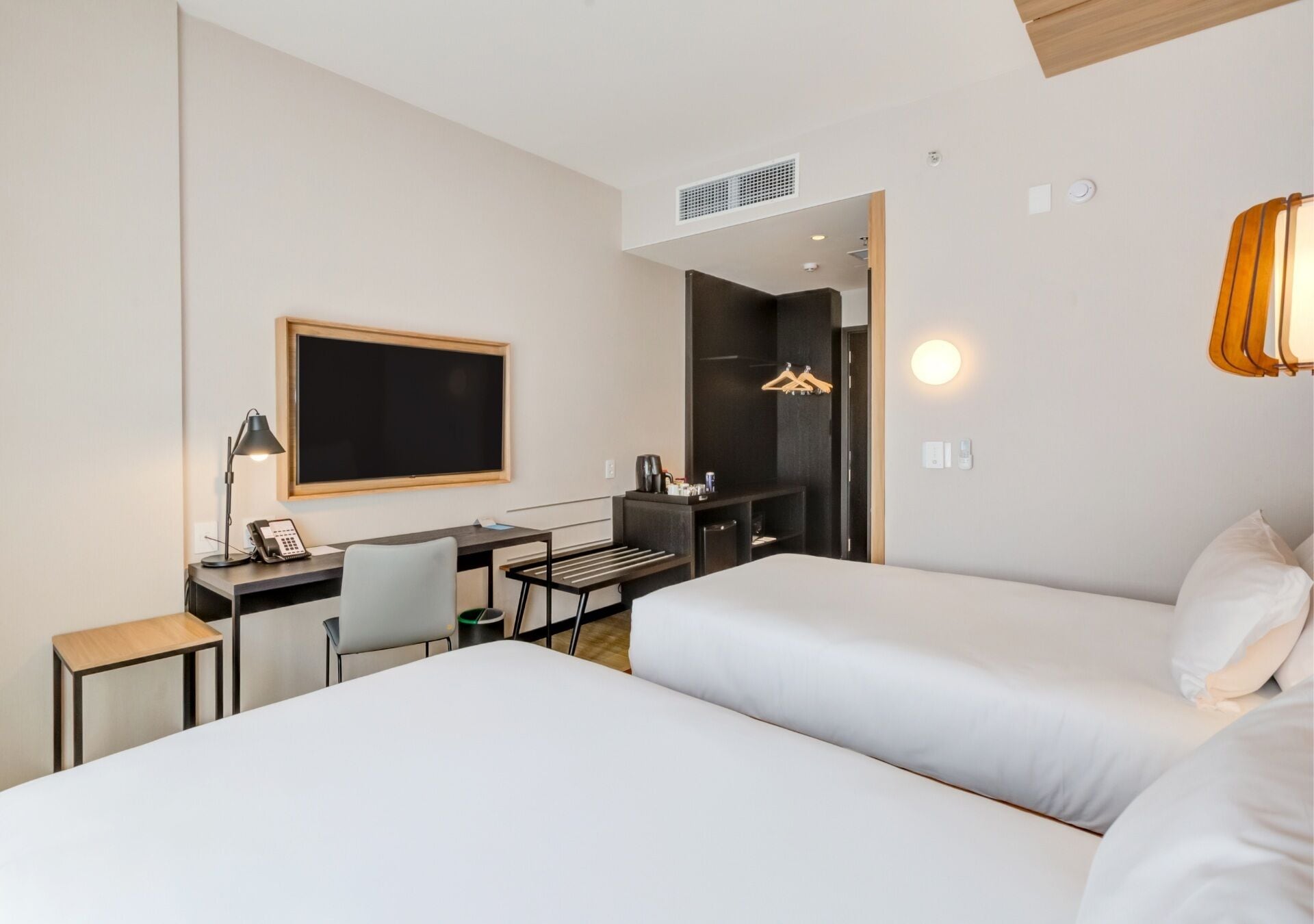 A hotel room with two beds, a desk with a chair, a TV, and a wardrobe.