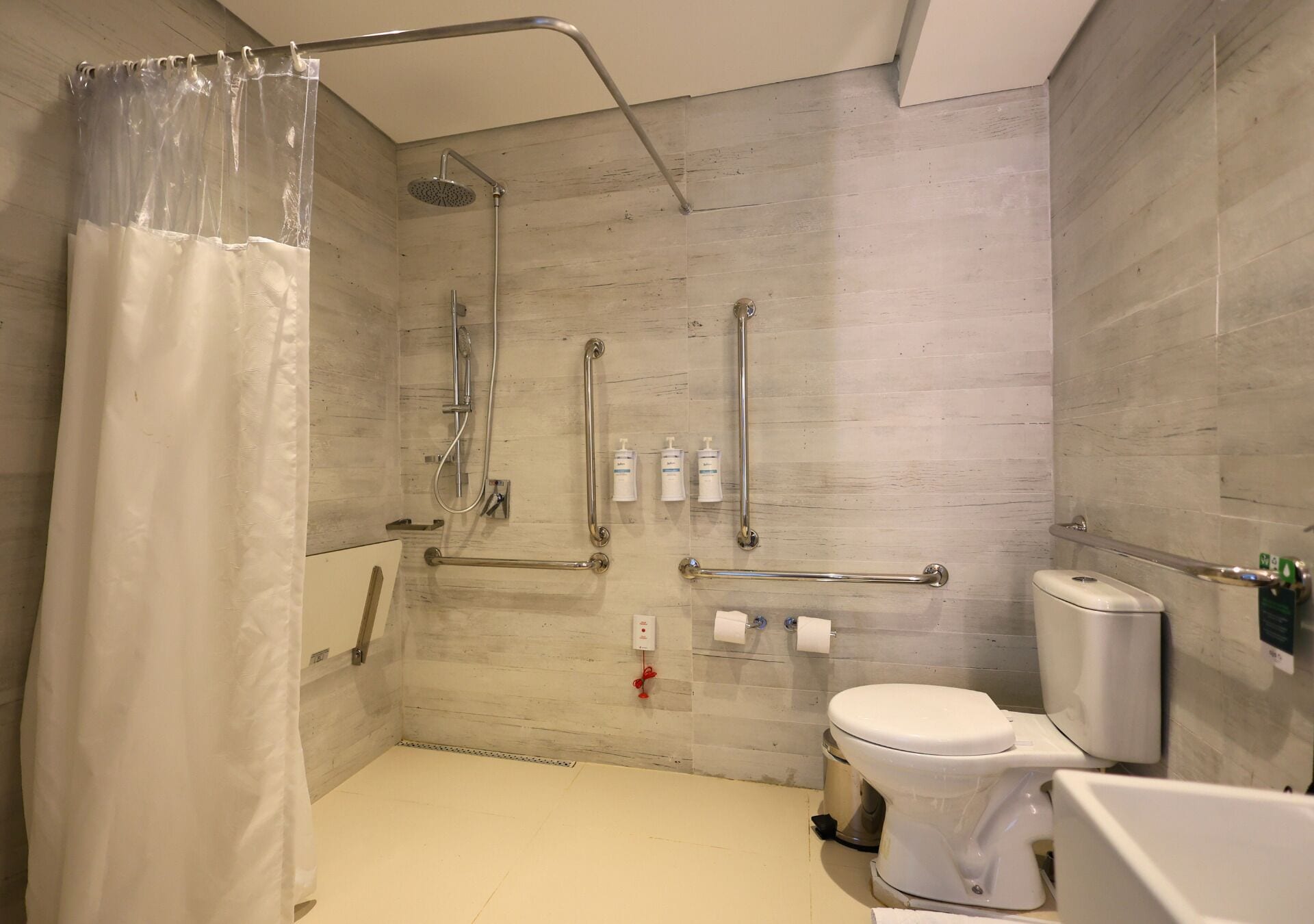 A modern bathroom with a shower, toilet, and bathtub. It features grab bars, a hand dryer, and a soap dispenser.