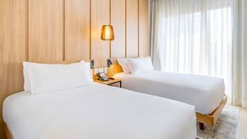 Habitación de hotel con dos camas, una pared de paneles de madera, una lámpara de noche y una ventana con cortinas.