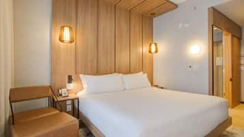 A hotel room with a large bed, a wooden headboard, two bedside lamps, a nightstand with a phone, and a brown leather chair.
