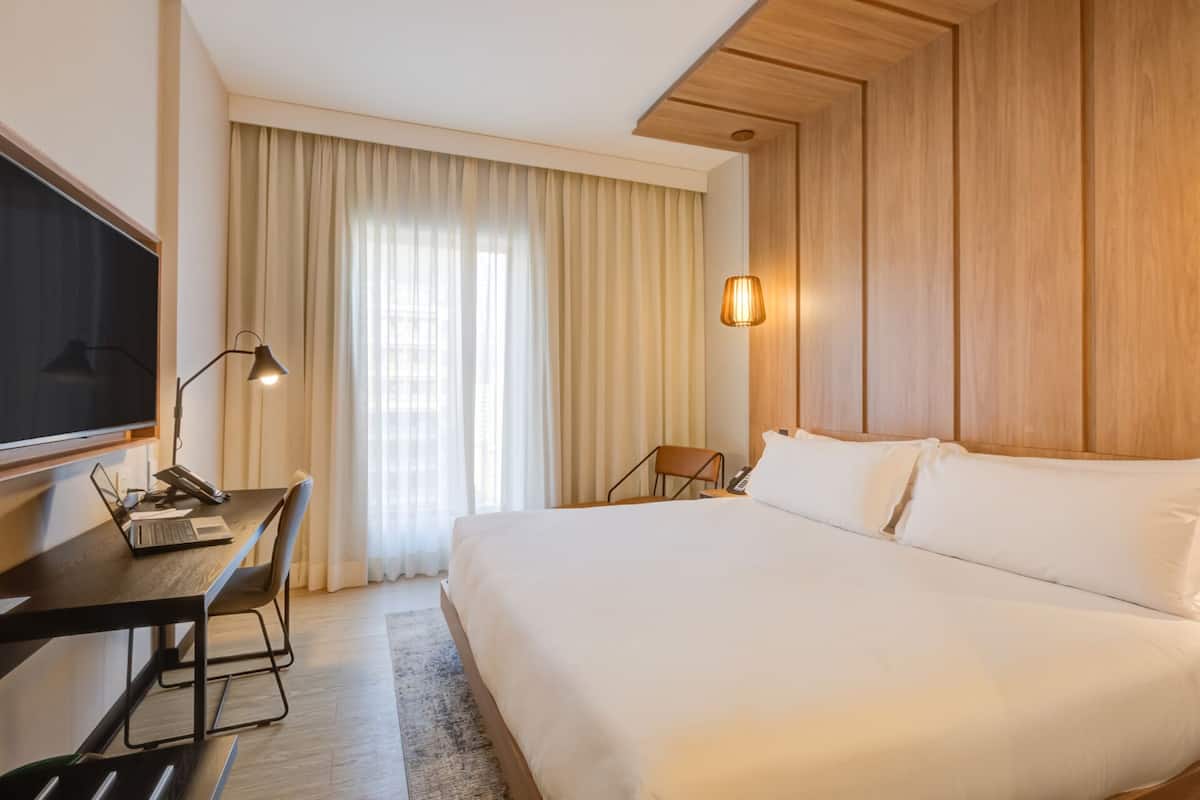Une chambre d’hôtel avec un grand lit, un bureau avec un ordinateur, une télévision et une lampe.