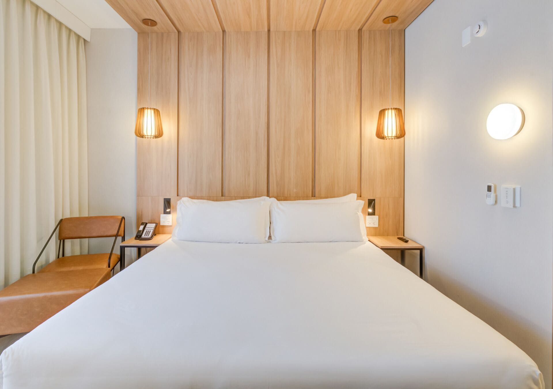 A hotel room with a large bed, two bedside lamps, a chair, a bedside phone, and a wall-mounted light.