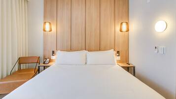 A hotel room with a large bed, two bedside lamps, a chair, a bedside phone, and a wall-mounted light.