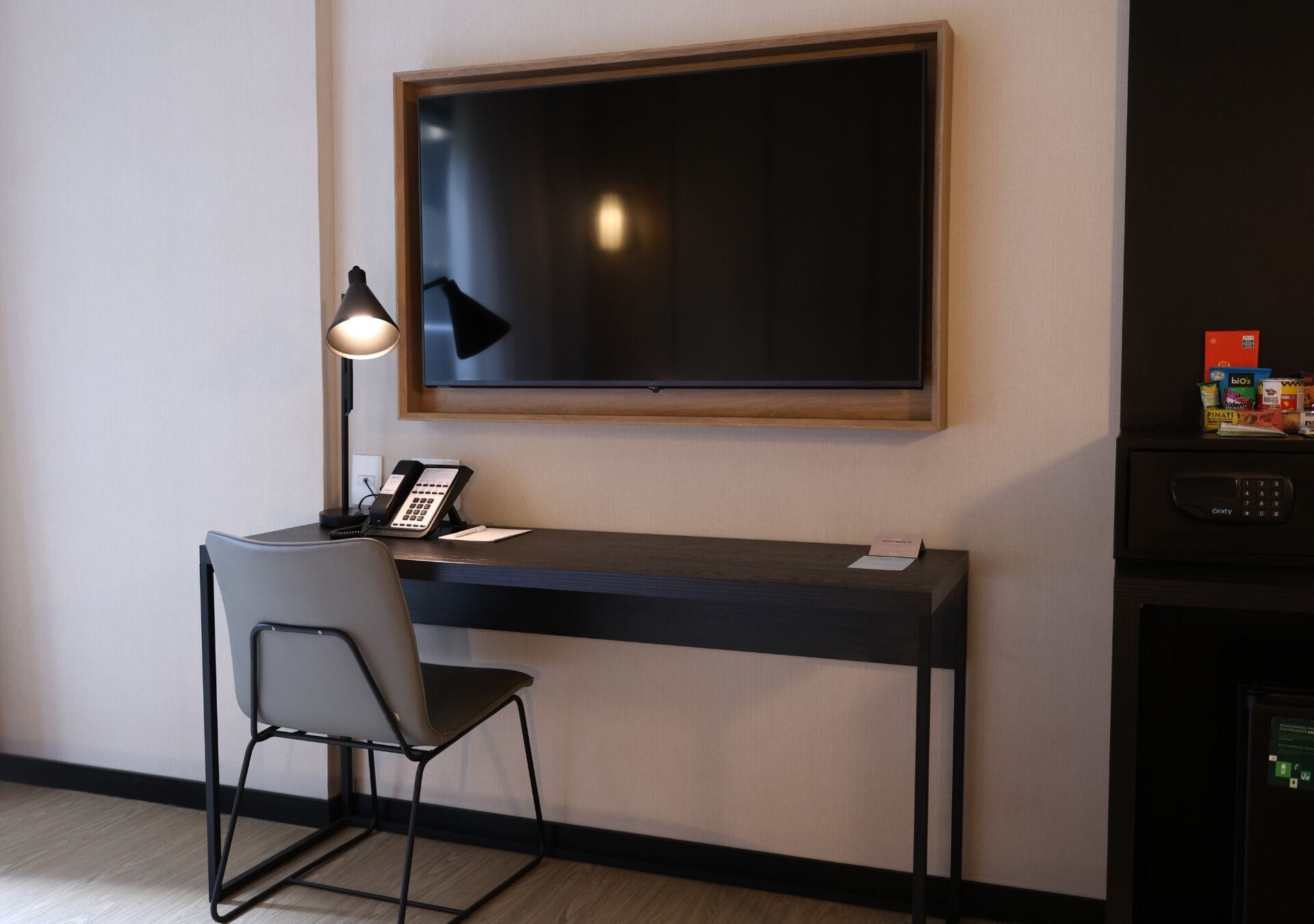 A hotel room with a desk, a chair, a telephone, and a television mounted on the wall.