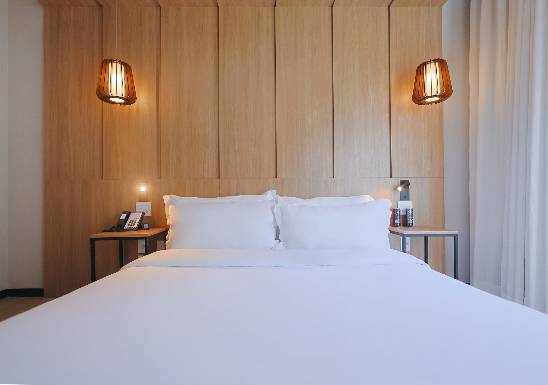 A hotel room with a large bed, two bedside tables, a telephone, and two wall-mounted lamps.