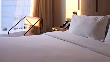 A hotel room with a bed, a chair, a bedside table with a phone, and a window with curtains.