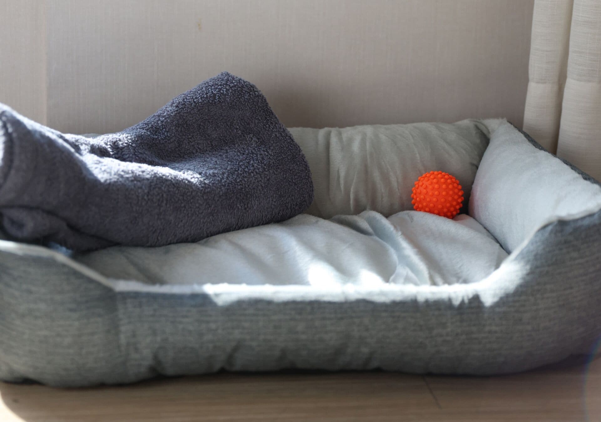 Una cama para mascotas con una manta gris y un juguete naranja.