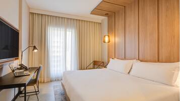 A hotel room with a large bed, a desk with a laptop, a chair, a TV, and a window with curtains.