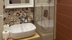 Ein Badezimmer mit weißem Waschbecken, einem Spiegel, einer Dusche und Fliesen mit Muster.