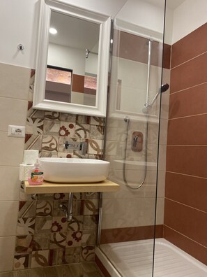 Ein Badezimmer mit weißem Waschbecken, einem Spiegel, einer Dusche und Fliesen mit Muster.