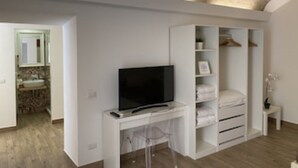 Ein modernes Zimmer mit einem Fernseher auf einem weißen Schreibtisch, einem begehbaren Kleiderschrank mit Regalen und Ablageflächen sowie einer Steinwand.