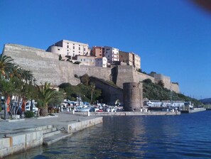 A coastal town with a prominent castle on a hill, a marina with boats, and a clear blue sky.