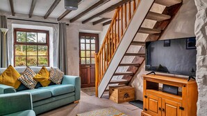 Een woonkamer met een bank, televisie, houten kast en een trap.