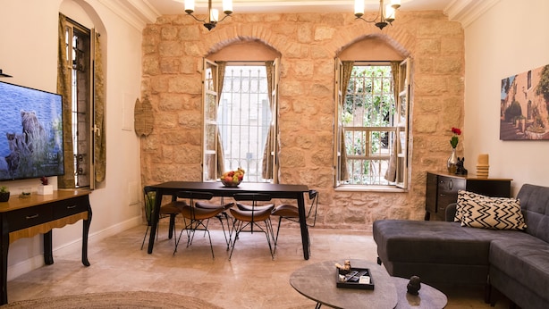A spacious living room with a stone wall, a chandelier, a dining area with a table and chairs, and a sofa. - Tish ApartHotel (Jerusalem)