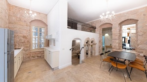 A spacious kitchen with stone walls, a dining area with a table and chairs, and a staircase leading to an upper level. - Tish ApartHotel (Jerusalem)