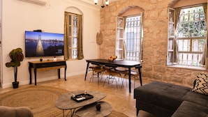 A living room with a TV, dining table, chairs, sofas, and a stone wall. - Tish ApartHotel (Jerusalem)