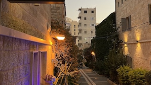 A TISH Hotel sign, stone buildings, a paved walkway, and a dog walking. - Tish ApartHotel (Jerusalem)