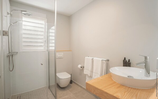 A modern bathroom with a glass-enclosed shower, a toilet, and a wooden vanity with a sink.